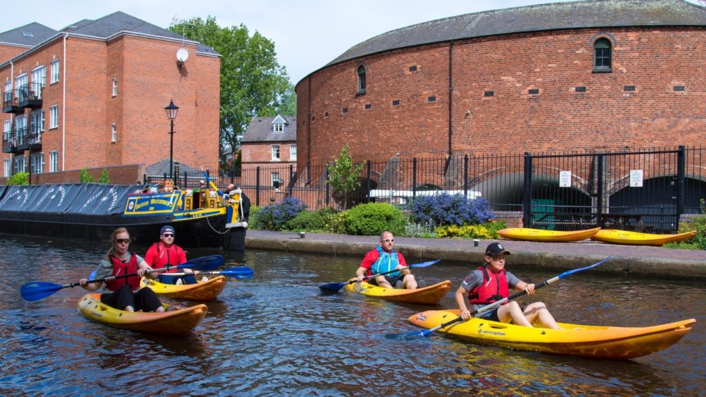 Four Roundhouse kayakers on the canal outside the Roundhouse on a sunny day.