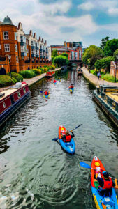 Picture of several Roundhouse kayakers on the canal heading towards the Roundhouse past Lego Birmingham. On both sides of the wide canal there are several moored narrowboats