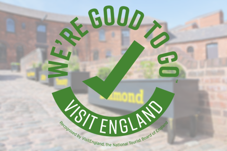 Good to go logo. Green writing in a round shape . It reads - We're good to go visit England . Recognised by VisitEngland, The National Tourist Board of England . The logo is stamped on a faded picture of the Roundhouse courtyard.