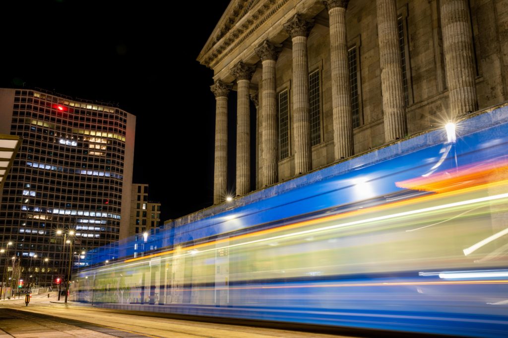 Light Trail by Ahsen Sayeed. A photograph taken at night outside Town Hall Birmingham A band of colourful light in shades of yellow and blue wraps the bottom half of the Town Hall.