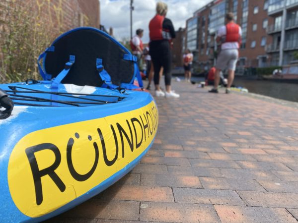 Picture of a Roundhouse kayak ready for launch on the path outside the Roundhouse. In the distance out of focus, kayakers in water jackets are getting in the kayaks