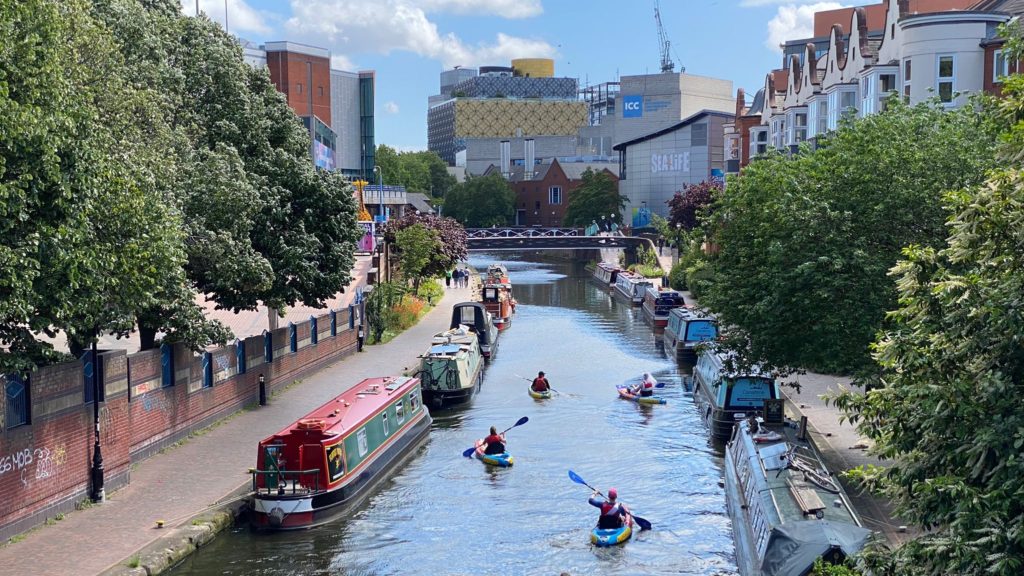 A group of people kayak up the canal towards Birmingham Library on a tour with Roundhouse Birmingham