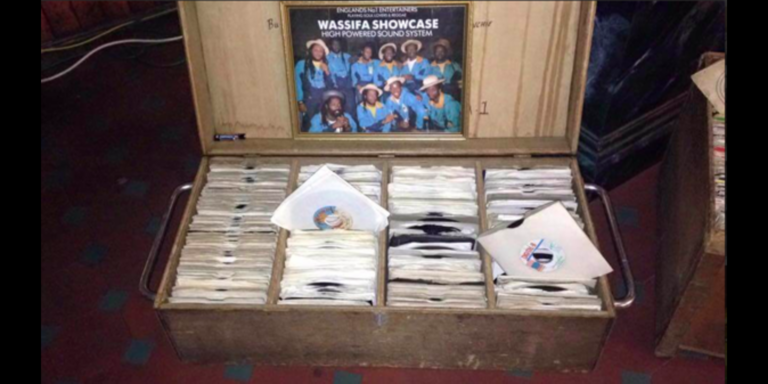 Picture of a wooden box filled with vinyl disks of Wassif Showcase . The box has a picture of The Wassif Sound System band.