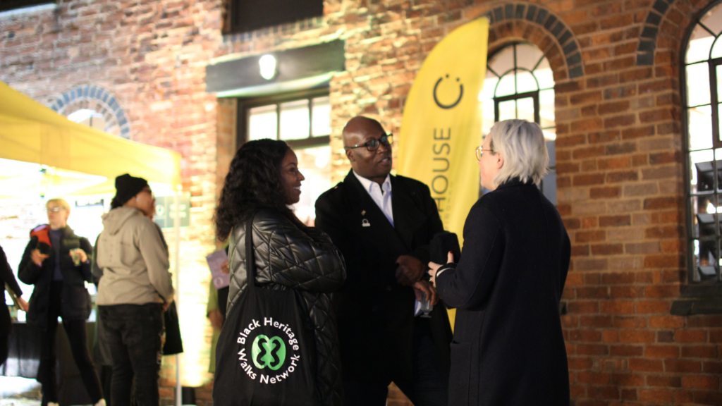 Picture of several people black and white chatting at the launch of My Voice My Path Audio Tour Launch. This was an evening event held in the Roundhouse courtyard.