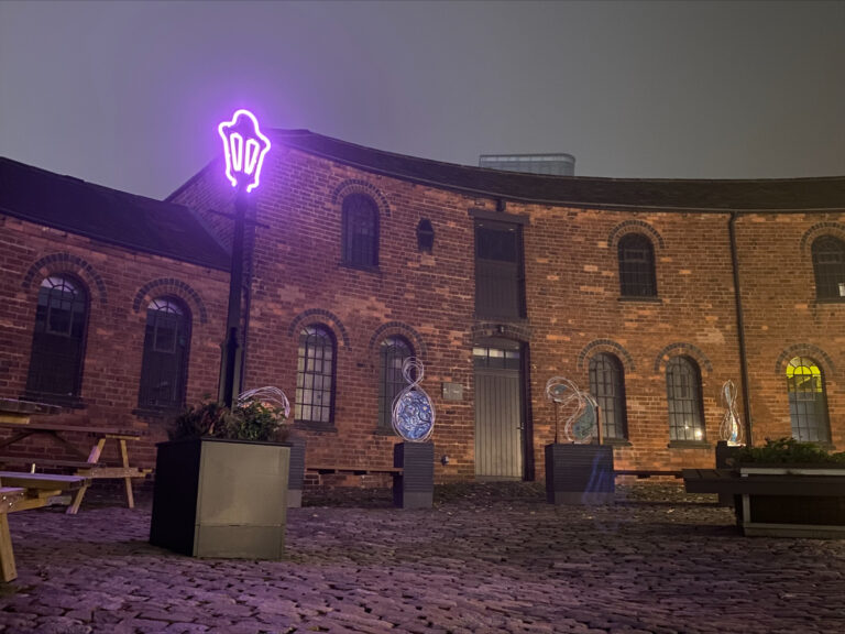 Picture of the Roundhouse courtyard in the dark with the Ladywood Light lit and several other glass and metal art pieces