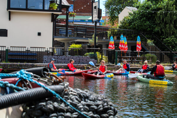 Group of Roundhouse kayakers on the water outside The Flapper Pub on a sunny day.