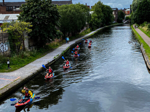 Group of Roundhouse kayakers moving down the canal closer to the photographer. The leader of the group is waving