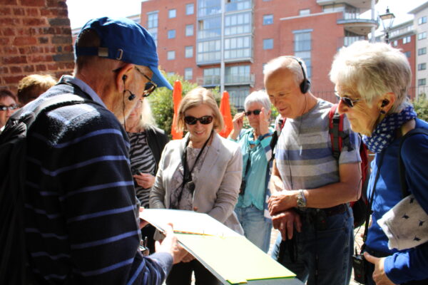 Group of visitors surrounding a Roundhouse tour guides who is showing a photograph