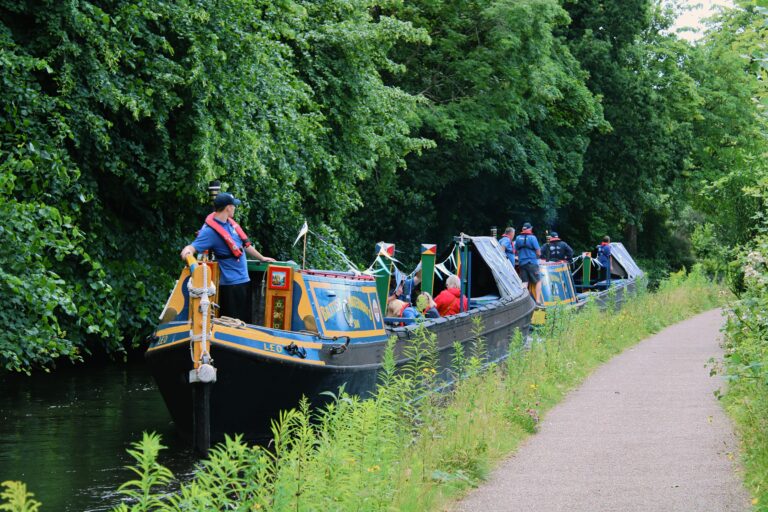 Two heritage working boats travelling through a narrow stretch of canal with lots of greenery on the offside