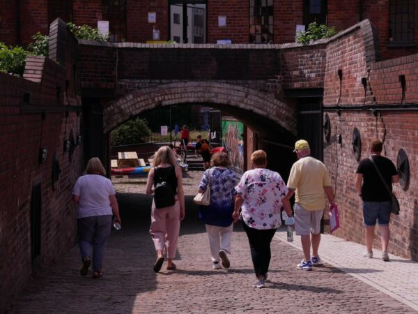 A landscape image showing a group of people walking down a cobbled path through an arched tunnel.