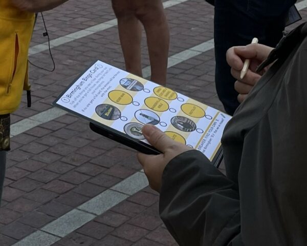 A landscape image showing someone holding a piece of paper. On the paper are 10 circles, some have images in, and some have words on a yellow background. The person is holding a pencil in their other hand.