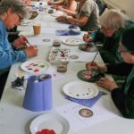 A photo of a long table with lots of people painting their rose and castle placemats
