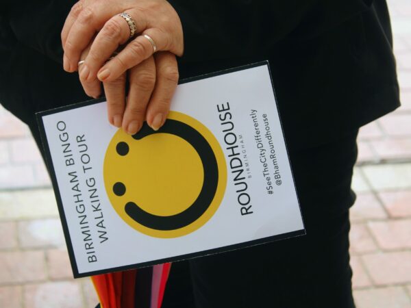 A landscape image showing a piece of card held in someone's hands. The card has a black smiling face on a yellow circular background.
