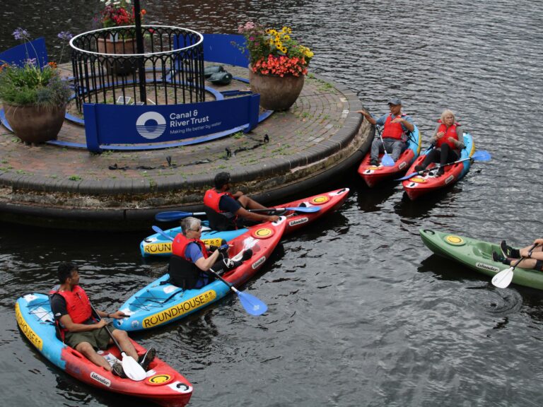 Group of kayakers, of mixed ages. gathered around canal roundabout.