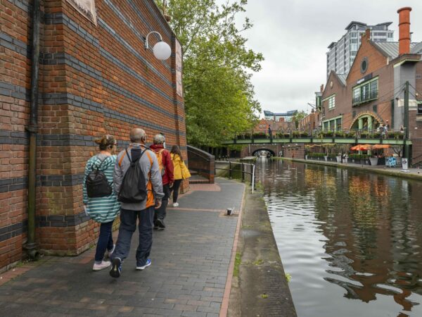 A landscape image showing three people being led by someone in a yellow jacket down a canal towpath. To their right is the canal.