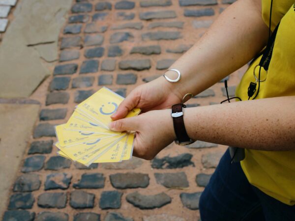 A landscape image showing a set of yellow cards with a black smiling face, fanned out in someone's hands. Cobbles are in the background.
