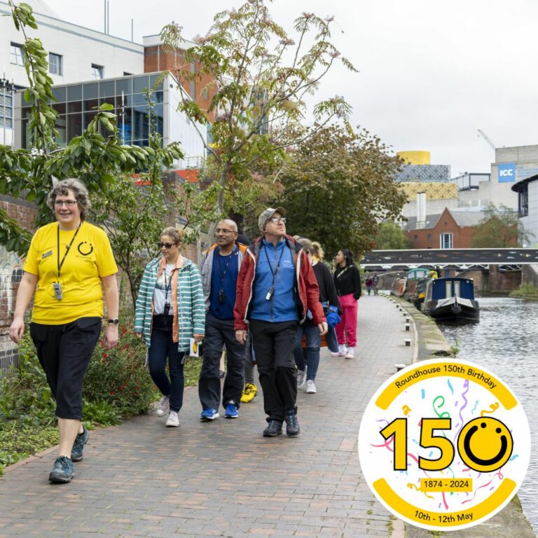 A square image showing a group of people walking along the canal on a towpath. They are following someone wearing a yellow t-shirt. In the bottom right of the image is a graphic logo with the number 150, the 0 of the logo is a yellow smiley face logo. The numbers 1 and 5 both have a black outline.