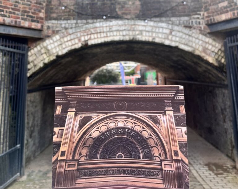 A landscape image showing someone holding a photo in front of a cobbled arched tunnel. The photo is of an etched wooden doorway with the name 'Shakespeare' etched around a semi circle arch.
