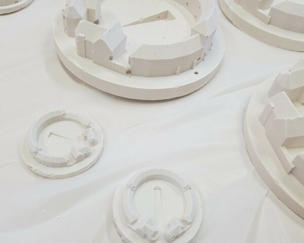 A landscape image showing some small models of a curved building. Theya re white and some are large, and the others are two small models. They are on a white table.