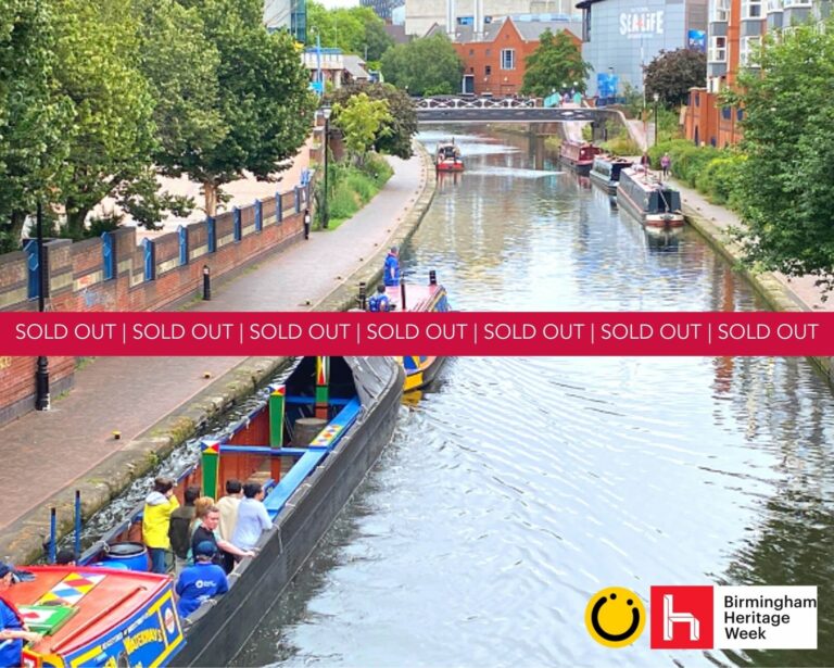 A landscape image showing a view of a canal. Either side of the canal is a path and, on the right, there are people walking along it. On the bottom left part of the image and on the canal is a red roofed and blue and yellow sided canal boat pulling a blue, black, green, red and yellow painted open air boat with 7 people stood on it. In the distance is a black and white metal bridge over the canal and other canal boats on the water. In the bottom right of the image is a yellow smiley face logo and a red square with the letter h in. Across the middle of the image is a red banner with the words sold out on.