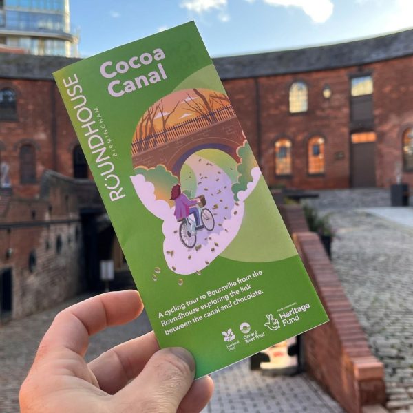 Picture of someone holding the Cocoa Canal Roundhouse illustration leaflet with the Roundhouse courtyard in the background