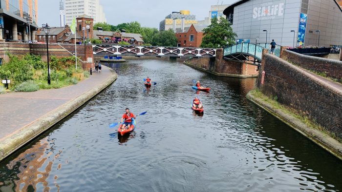 Four Roundhouse kayakers on the water kayaking passed Sea Life Birmingham building
