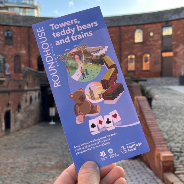 Picture of someone holding the Towers teddy bears and trains Roundhouse illustration leaflet with the Roundhouse courtyard in the background.
